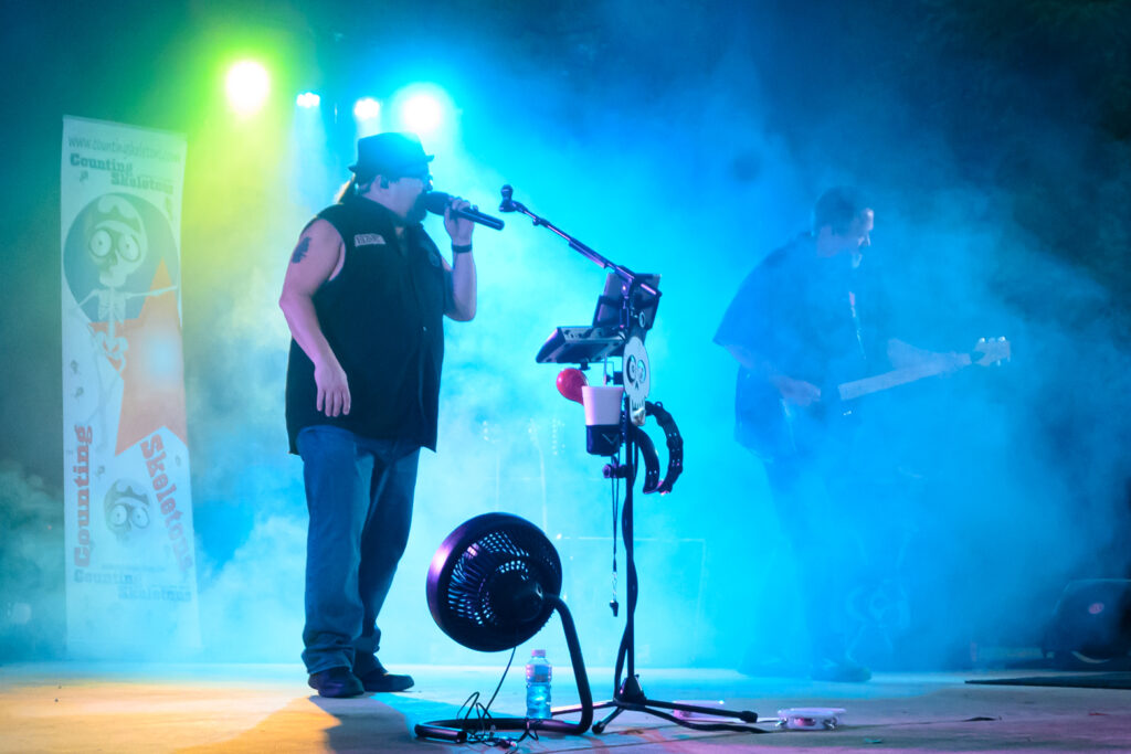 This photo features a lead singer with a microphone on a stage enveloped in smoke. A guitarist is barely visible in the smoke.
